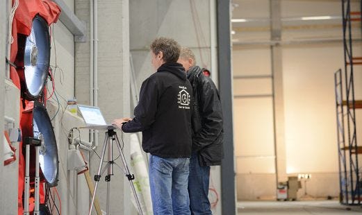 Zwei Männer stehen vor Blower Door Konstruktion und testen.